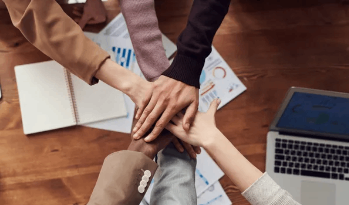 Hands of diverse people stacked together on a table with papers, notebook, and laptop.