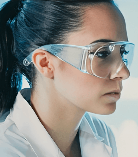 Woman in lab coat wearing safety glasses, looking intently.