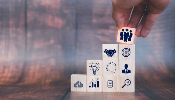 Hand placing team icon block atop a stack of blocks with business goal icons.