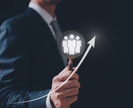 Businessperson holding magnifying glass over team icon with upward arrow, symbolizing growth.