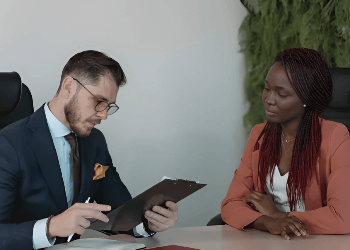 Man in suit reviewing documents with Black woman at a desk.