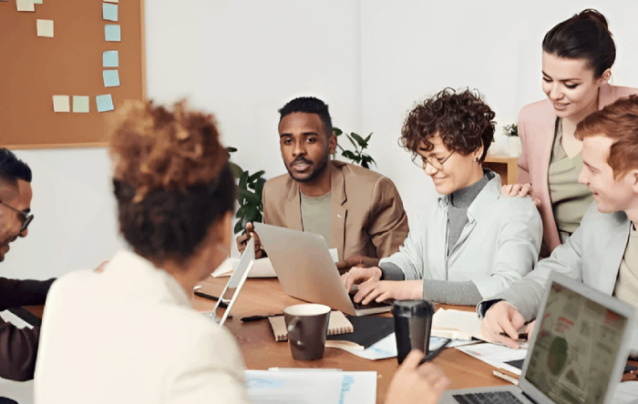 Group of diverse people at a table, working on laptops, brainstorming in an office setting.