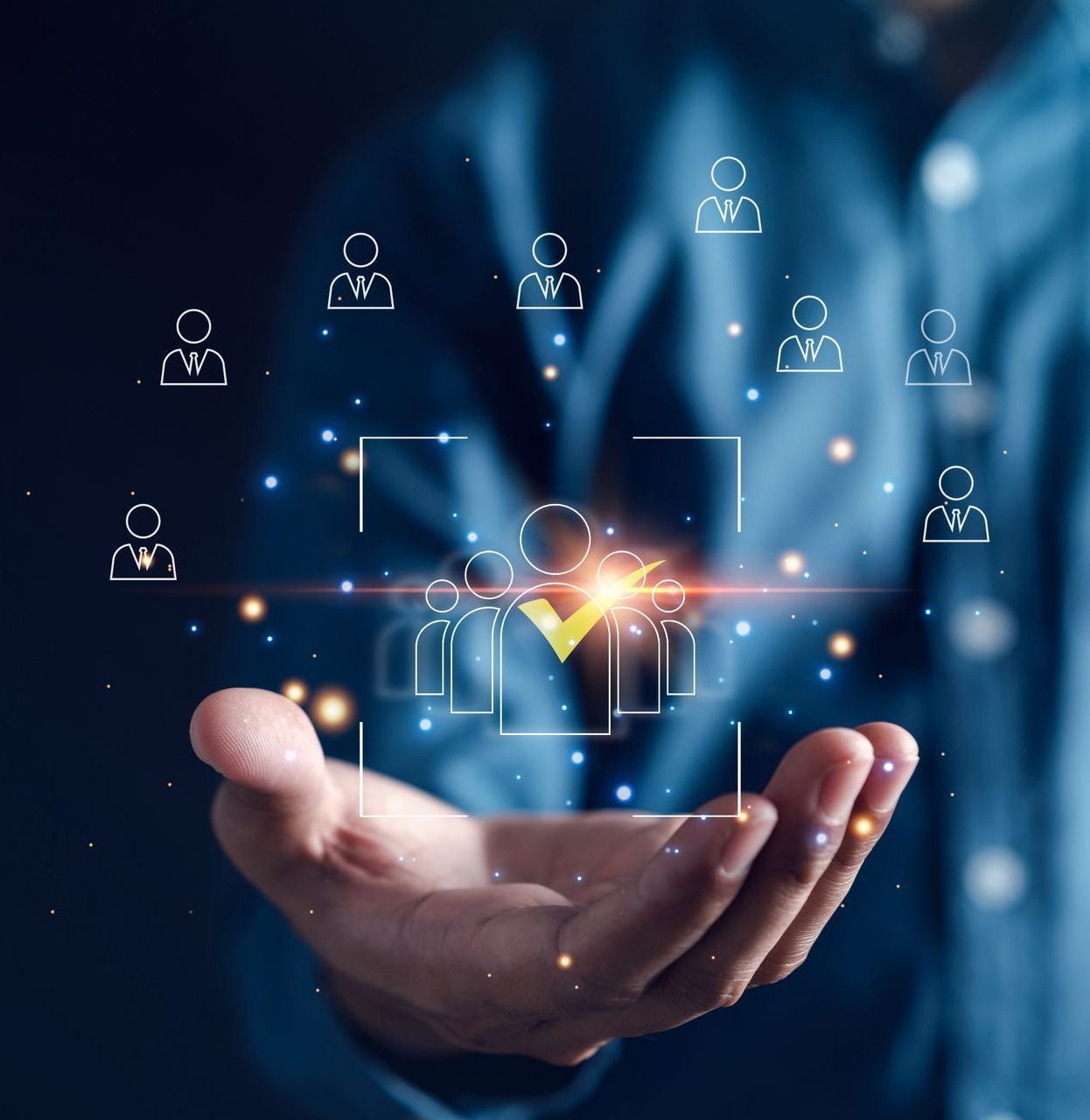 Man's hand holding a glowing graphic of people with a checkmark, representing recruitment and selection.