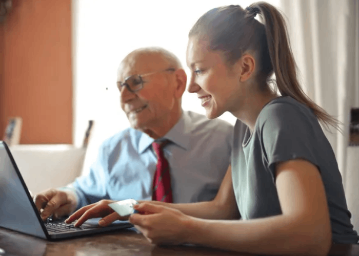 Young woman and older man smiling at a laptop, possibly shopping online. Woman holds a credit card.