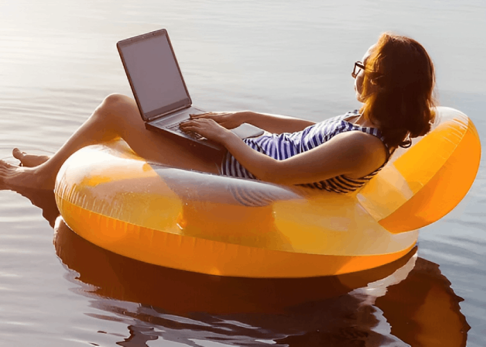 Woman in swimsuit using laptop while floating on inflatable raft in water.