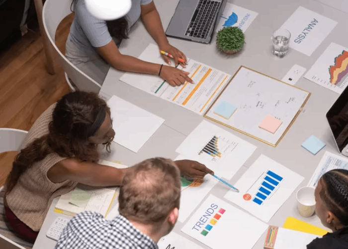 Business team reviewing charts and documents at a table, discussing trends and analysis.