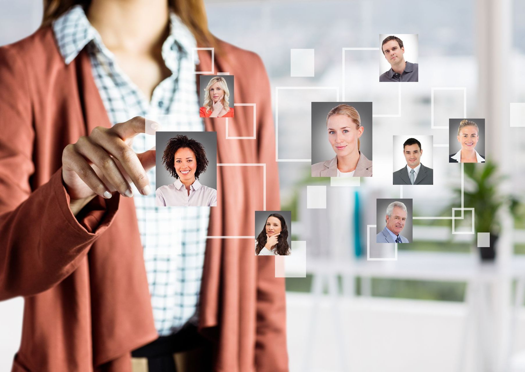 Woman in blazer touching a digital display of employee headshots; office setting.