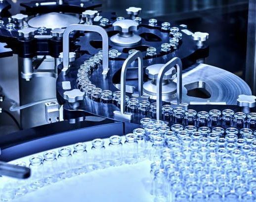 Automated machine filling glass vials with liquid, likely medication, in a factory setting.
