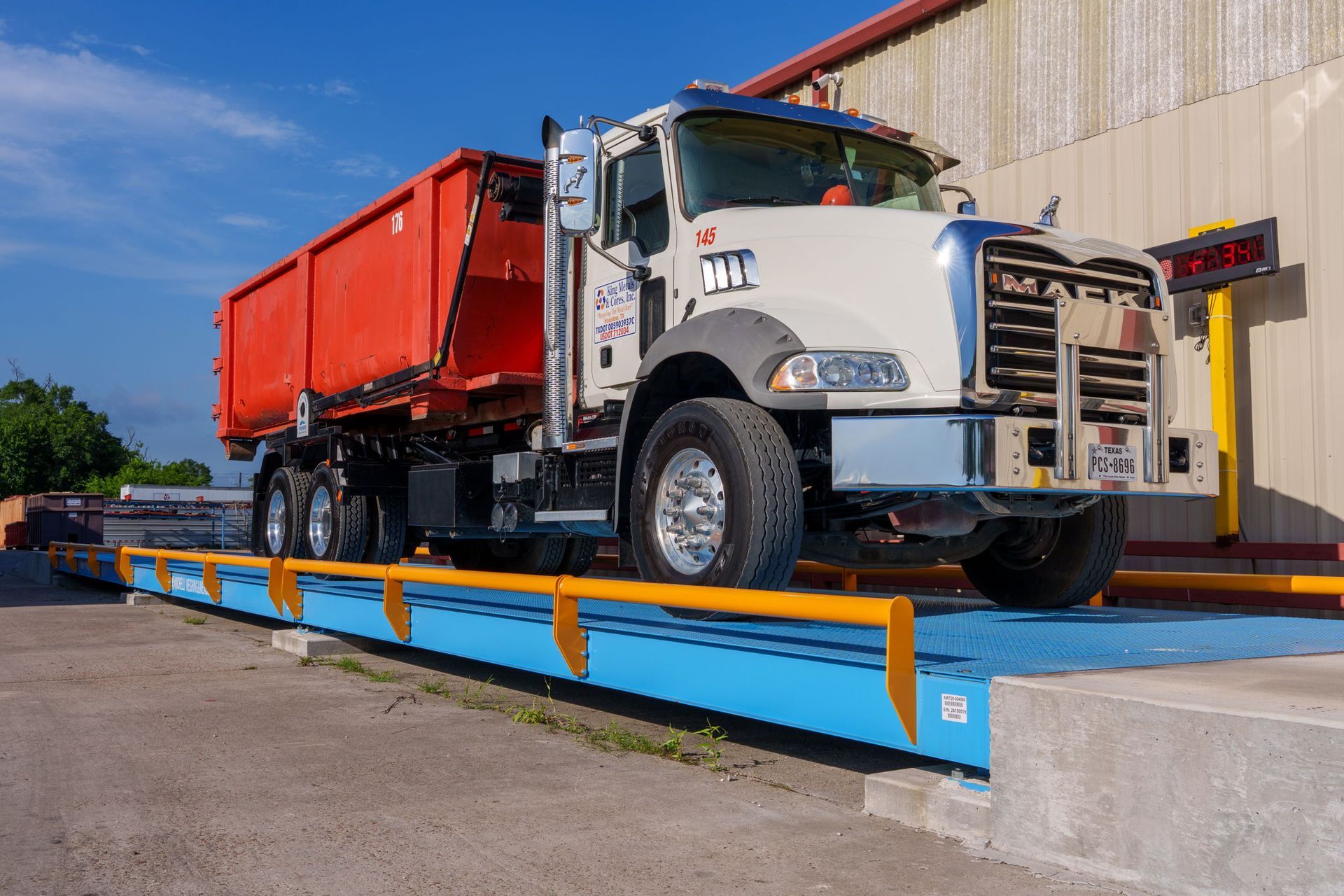 White dump truck on a blue weighbridge outside a warehouse