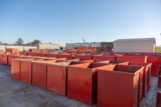 Rows of red metal dumpsters in an outdoor industrial yard under a clear sky