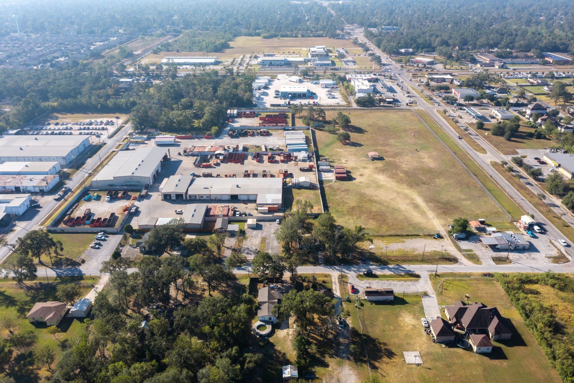 Aerial view of a suburban commercial area with roads, parking lots, buildings, and open fields.