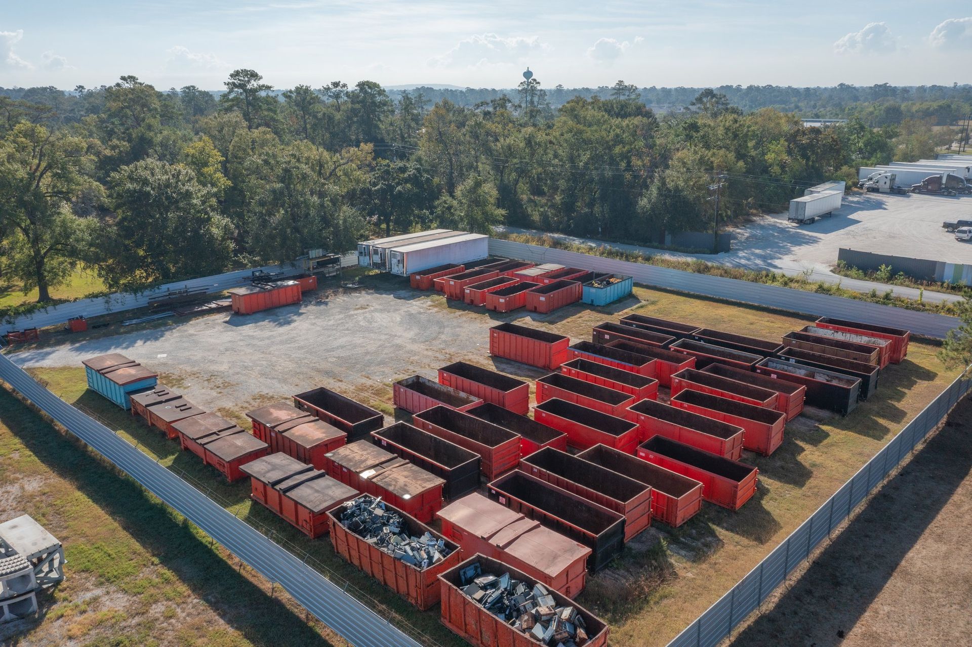 Aerial view of a yard filled with rows of red buses and trucks, surrounded by trees.