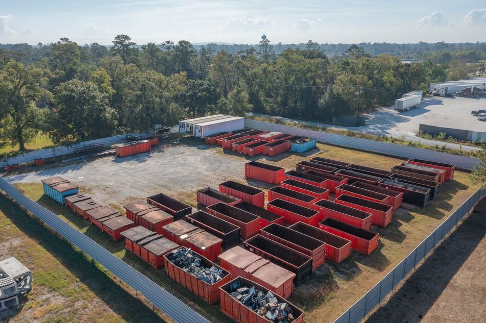 Aerial view of a yard filled with rows of red buses and trucks, surrounded by trees.