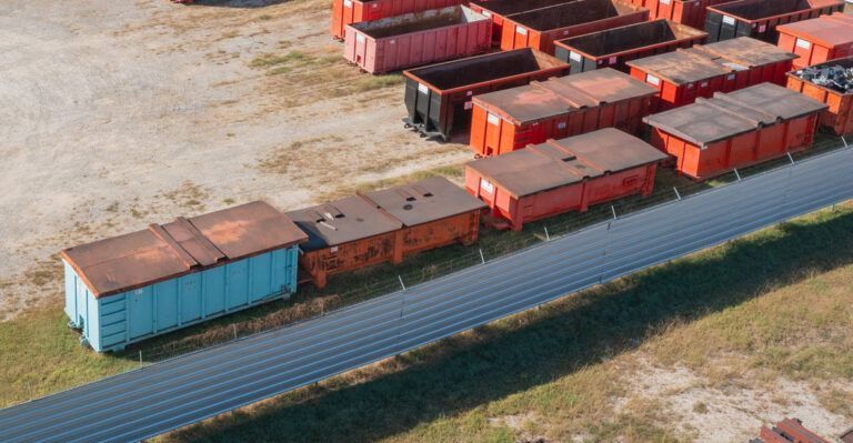 Aerial view of stacked shipping containers in a rail yard beside a blue fence
