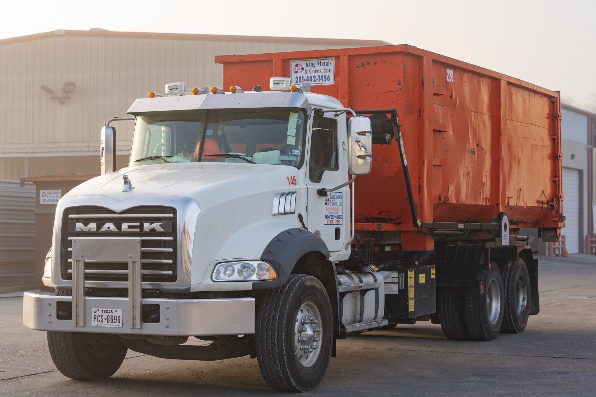 White Mack dump truck with orange bed parked outdoors in front of a building.