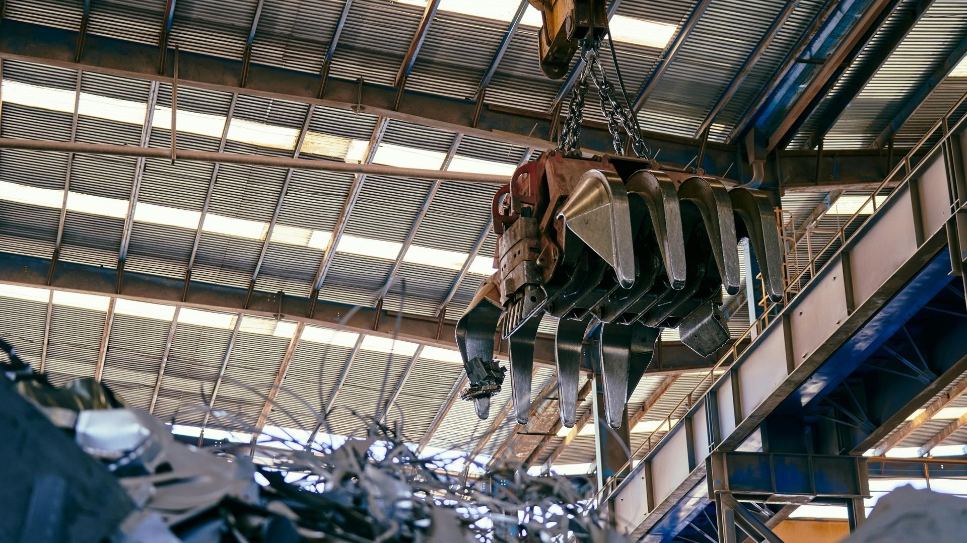 Large machine suspended inside an industrial warehouse with a corrugated metal roof and blue beams