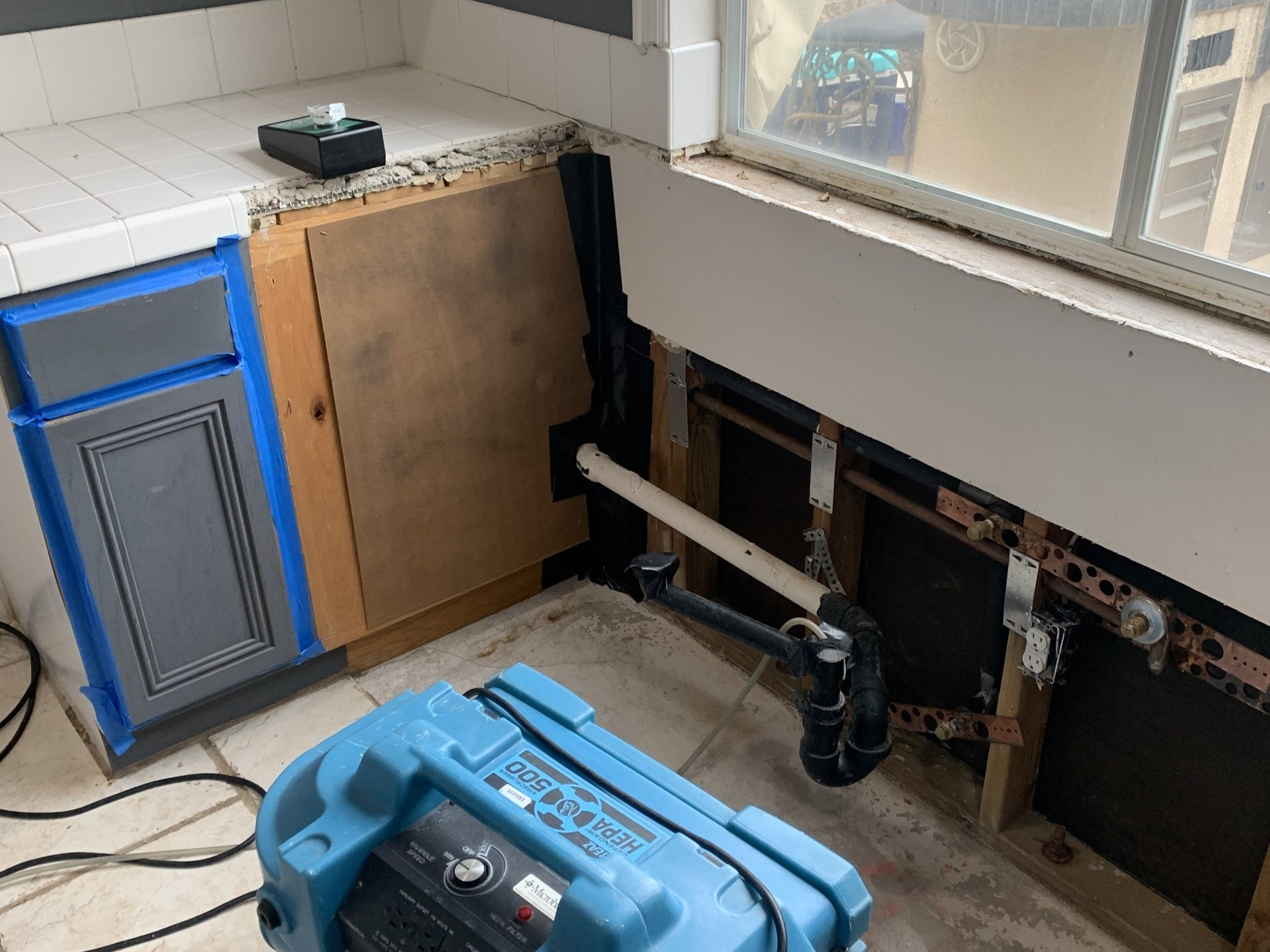 Partially dismantled wall with exposed plumbing, blue toolbox, and blue cabinet in a workshop area