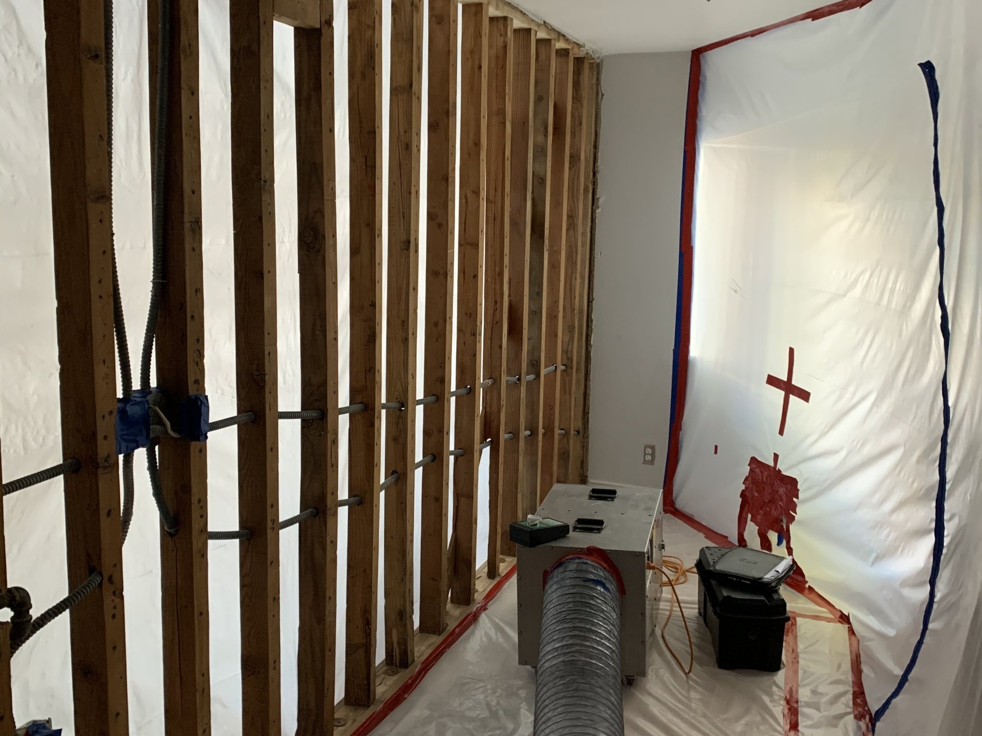 Partially built room with exposed wood studs, plastic sheeting, and tools on the floor