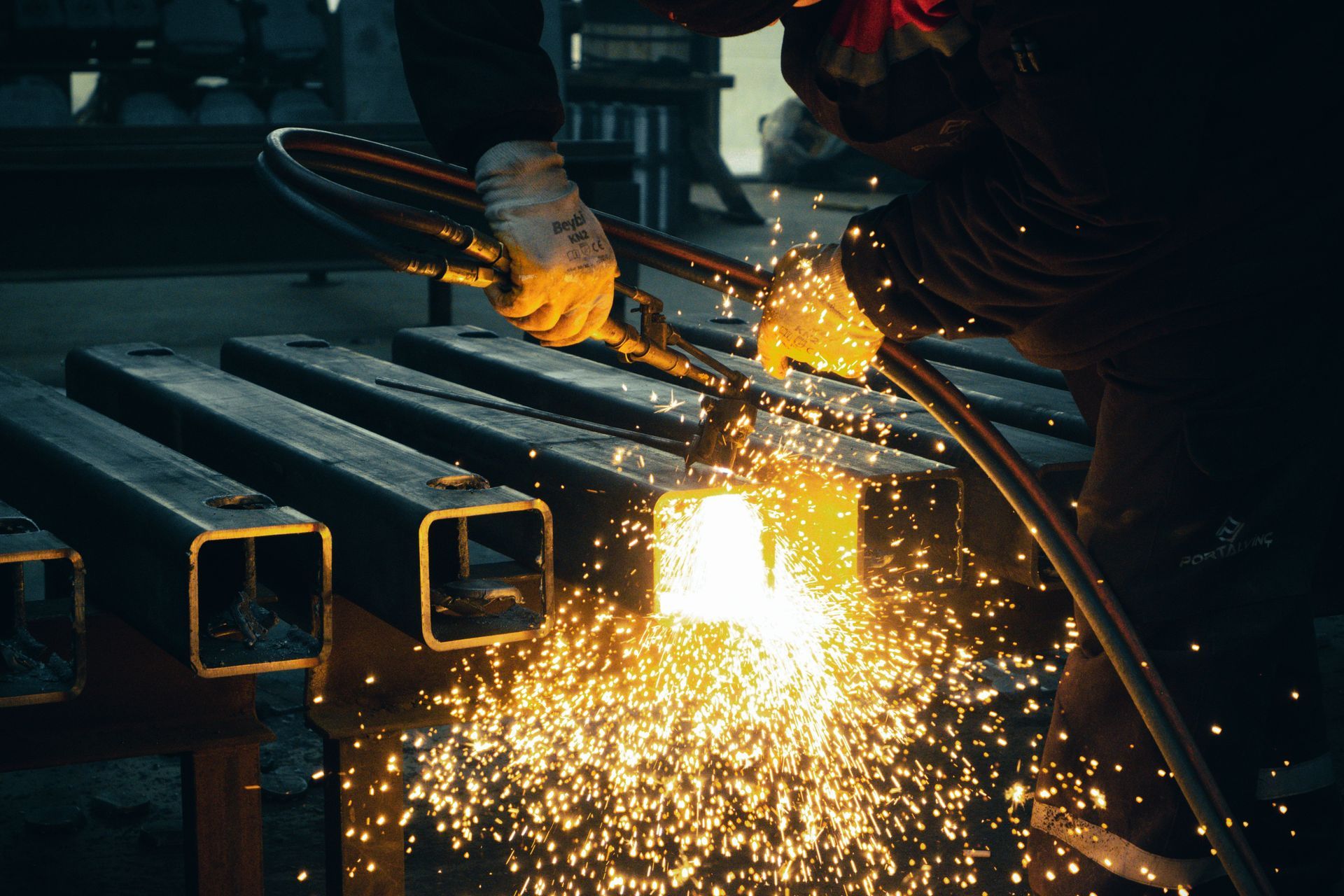 Worker cutting metal pipes with a grinder, sending bright sparks in a dim workshop
