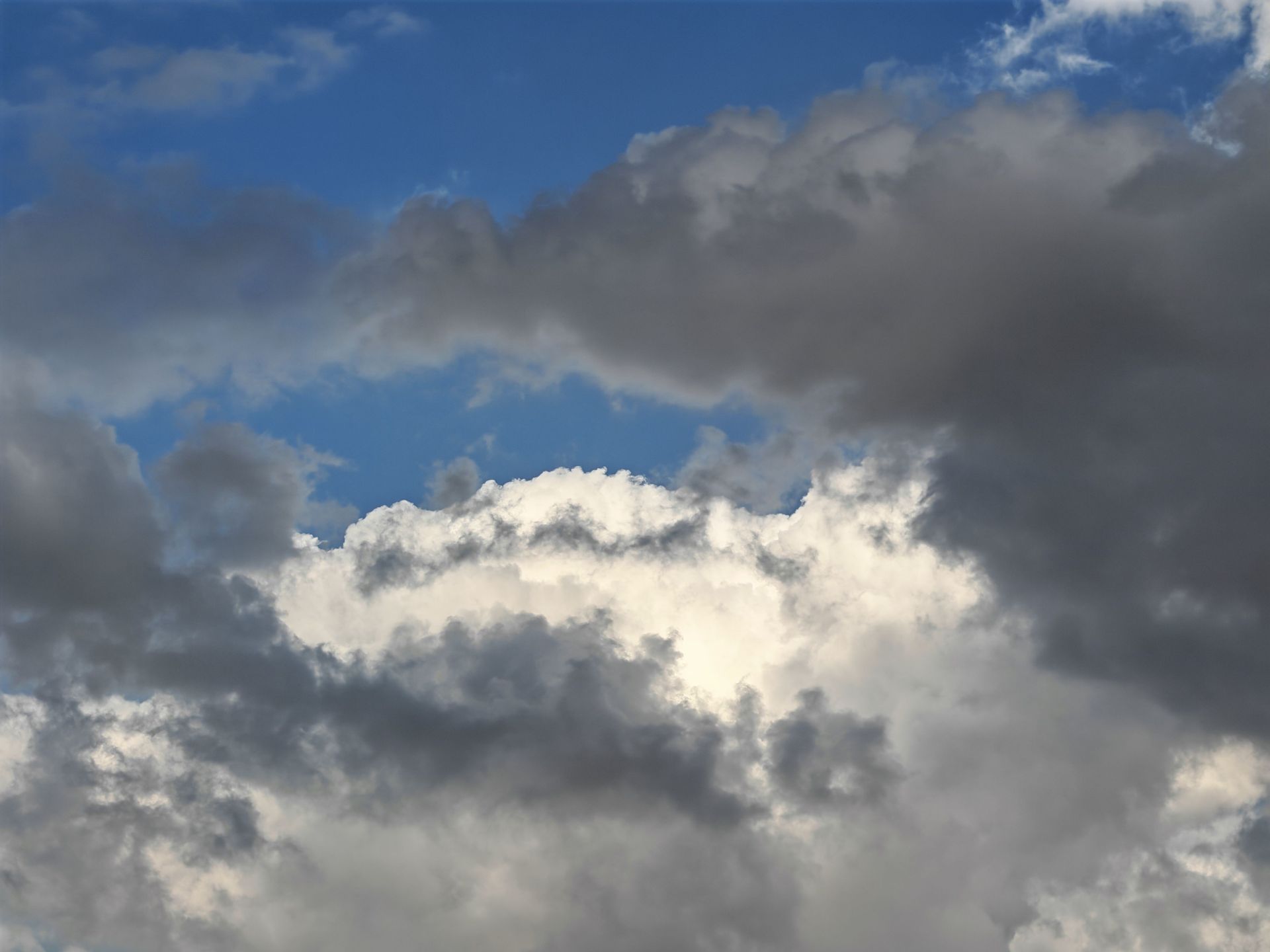 Dark and white clouds against a blue sky with sunlight breaking through