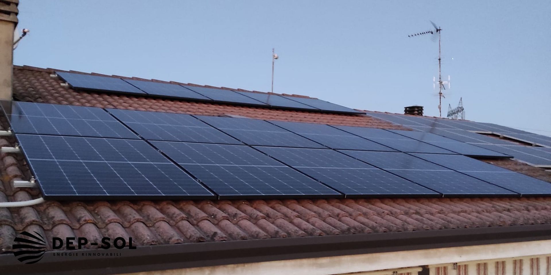 Pannelli solari installati su un tetto di tegole in terracotta, sotto un cielo sereno.