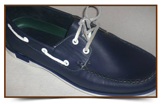 Zapato náutico azul marino con cordones y costuras blancas sobre fondo liso.