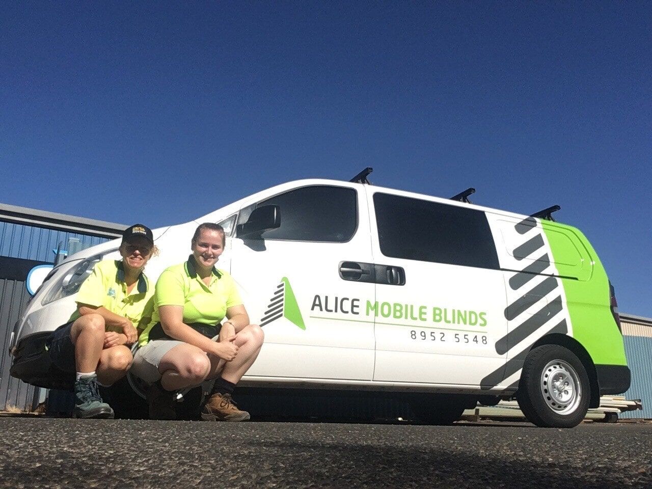 Two People Are Kneeling in Front of an Alice Mobile Blinds Van — Bluey's Signs in Ciccone, NT
