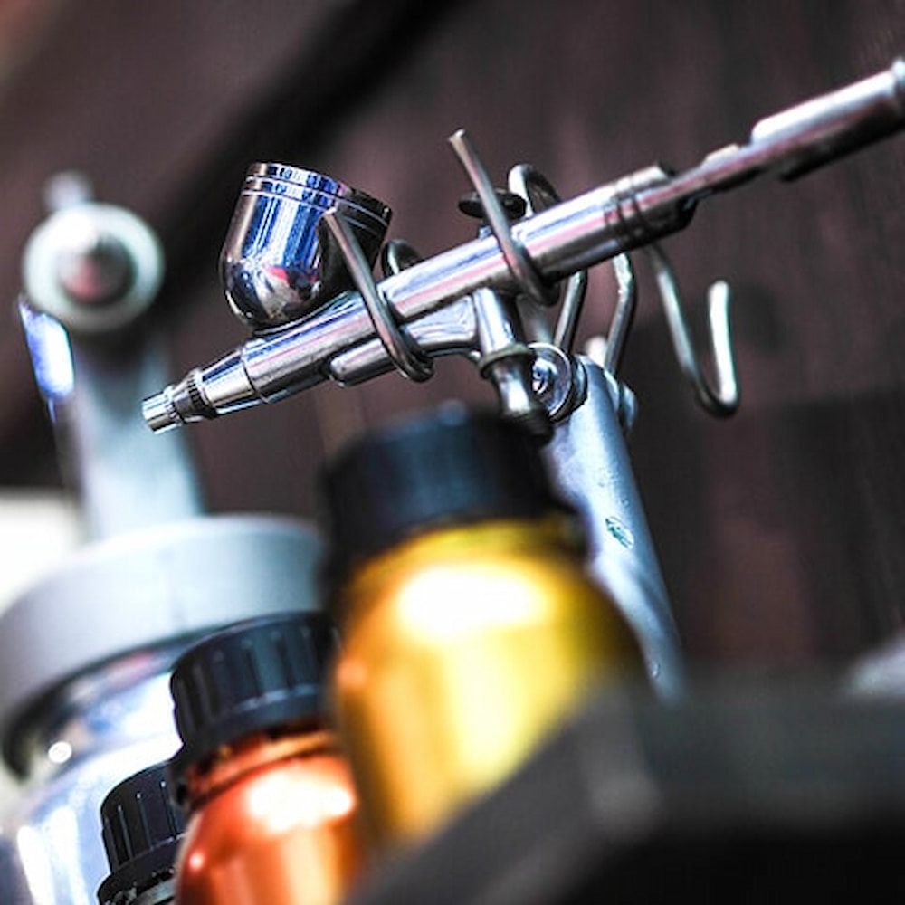A Close Up of an Airbrush With Bottles of Paint in the Background — Bluey's Signs in Ciccone, NT A Close Up of an Airbrush With Bottles of Paint in the Background — Bluey's Signs in Ciccone, NT