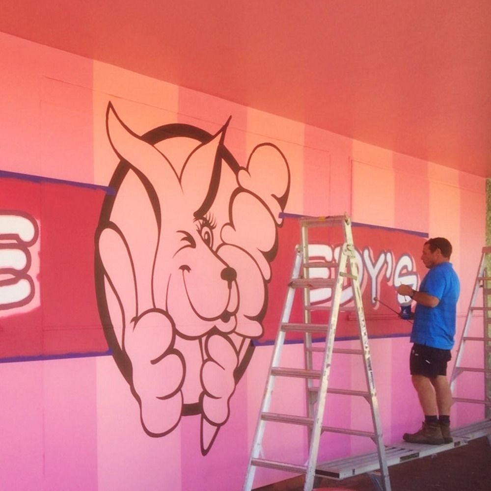 A Man on a Ladder is Painting a Bunny on a Pink Wall — Bluey's Signs in Ciccone, NT A Man on a Ladder is Painting a Bunny on a Pink Wall — Bluey's Signs in Ciccone, NT