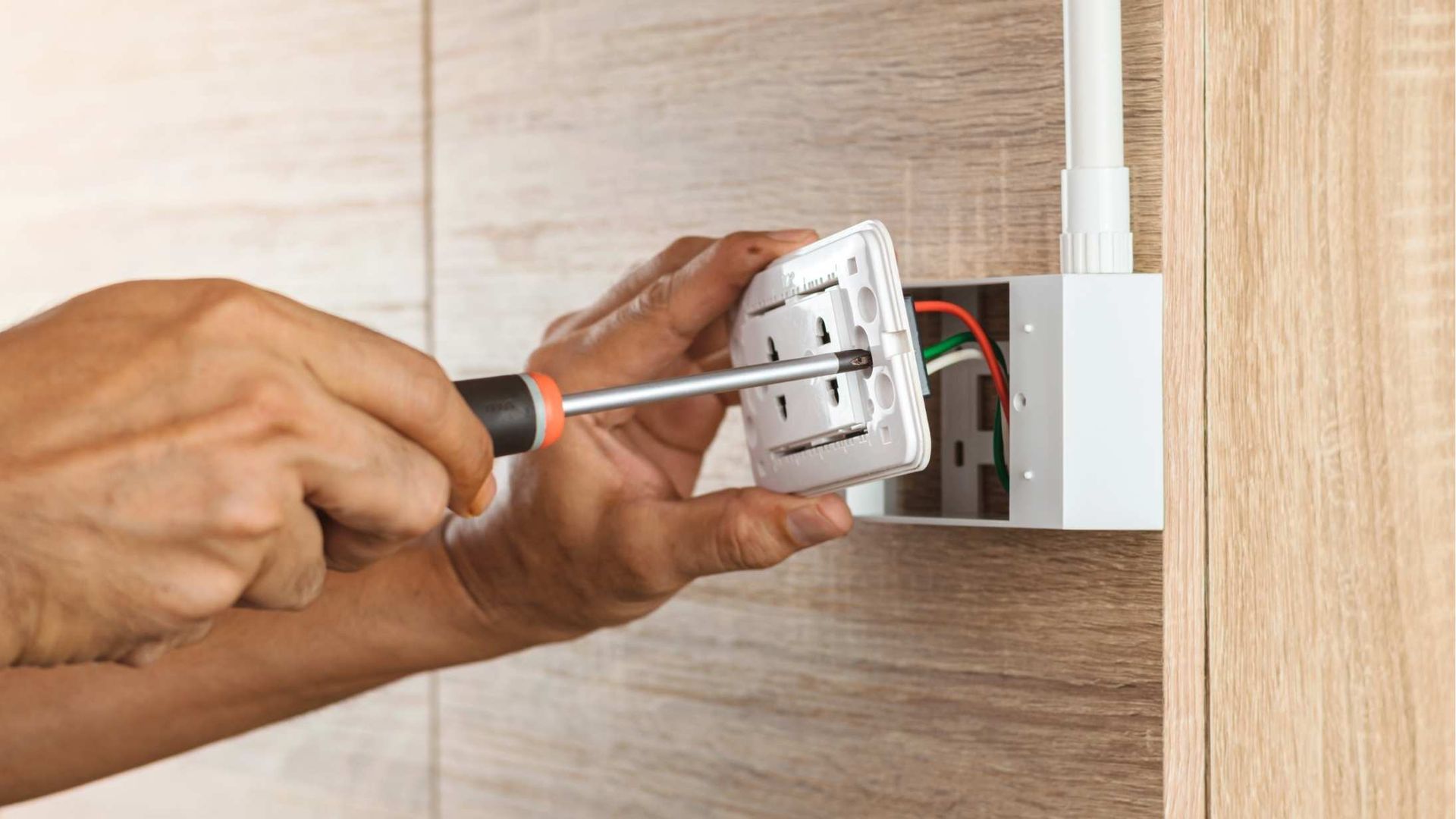 Hand using a screwdriver to work on an electrical wall outlet with exposed wiring