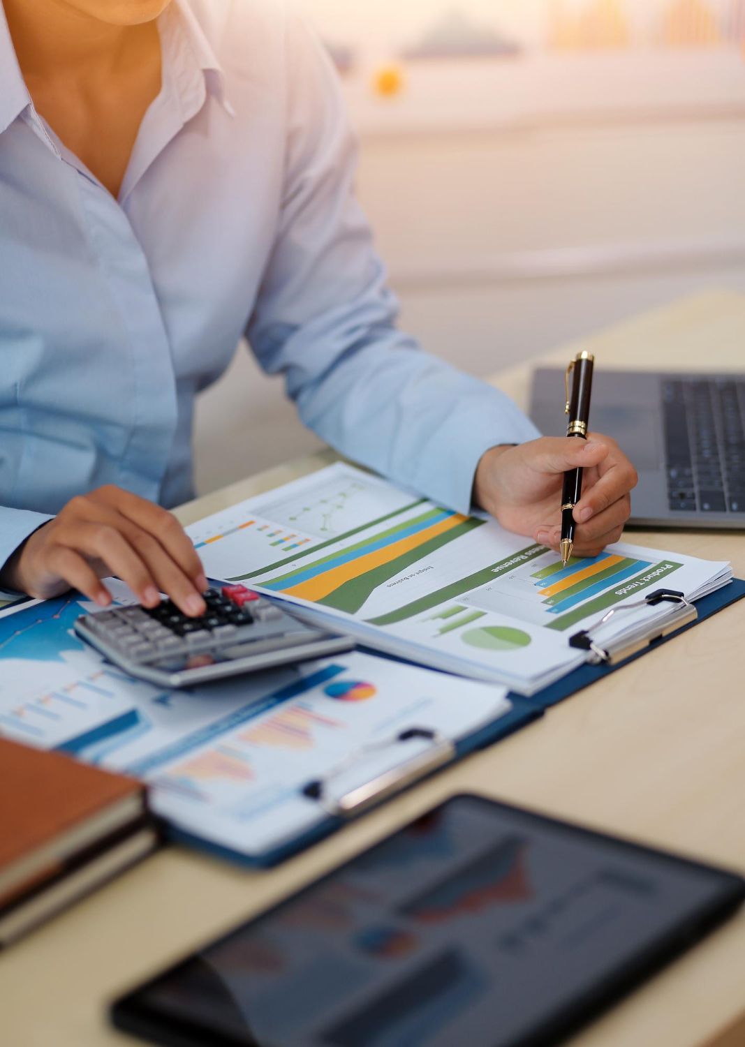 Person reviewing charts and writing in a notebook at a desk with a calculator and laptop