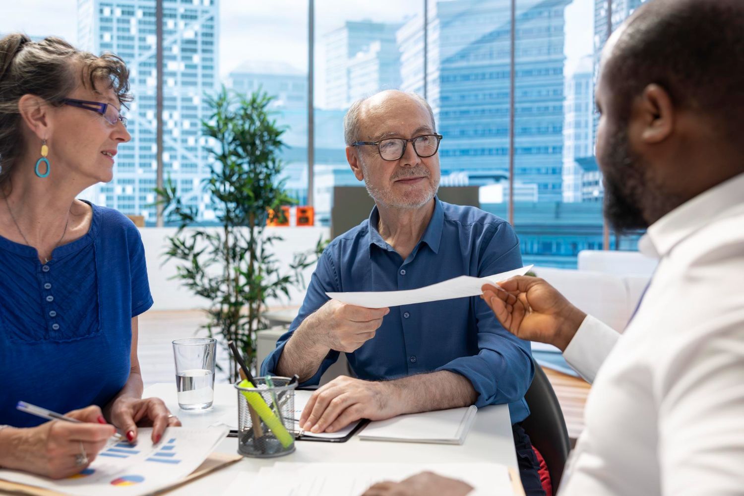 Three coworkers discussing documents at a conference table in a bright office meeting room