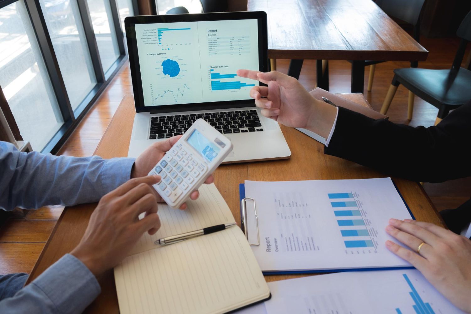 People reviewing financial charts on a laptop in a meeting, with one person holding a smartphone.