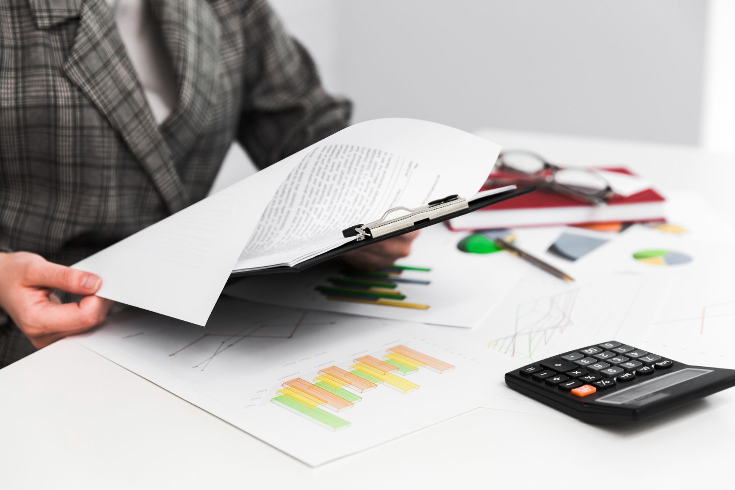 Person reviewing papers and charts at a desk with a calculator and colored pens.