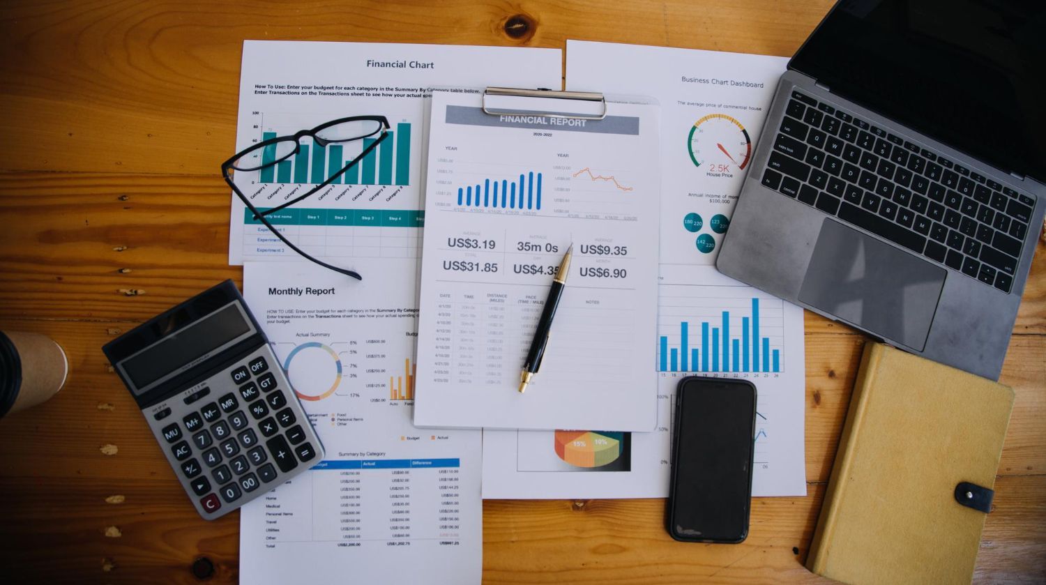 Overhead view of laptop, calculator, phone, and charts on a desk with pens and papers