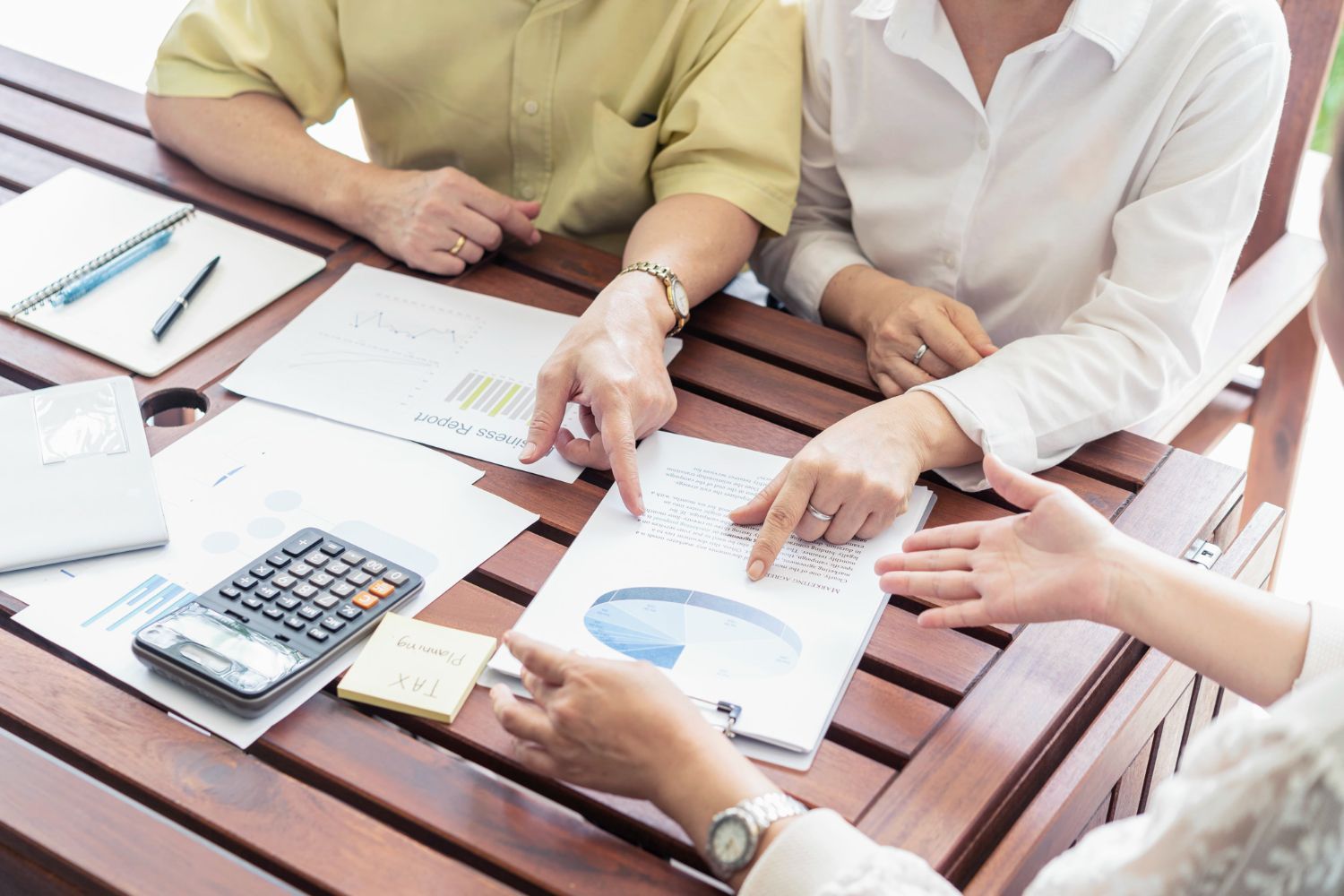 People reviewing charts and paperwork at a wooden table with calculator and pens
