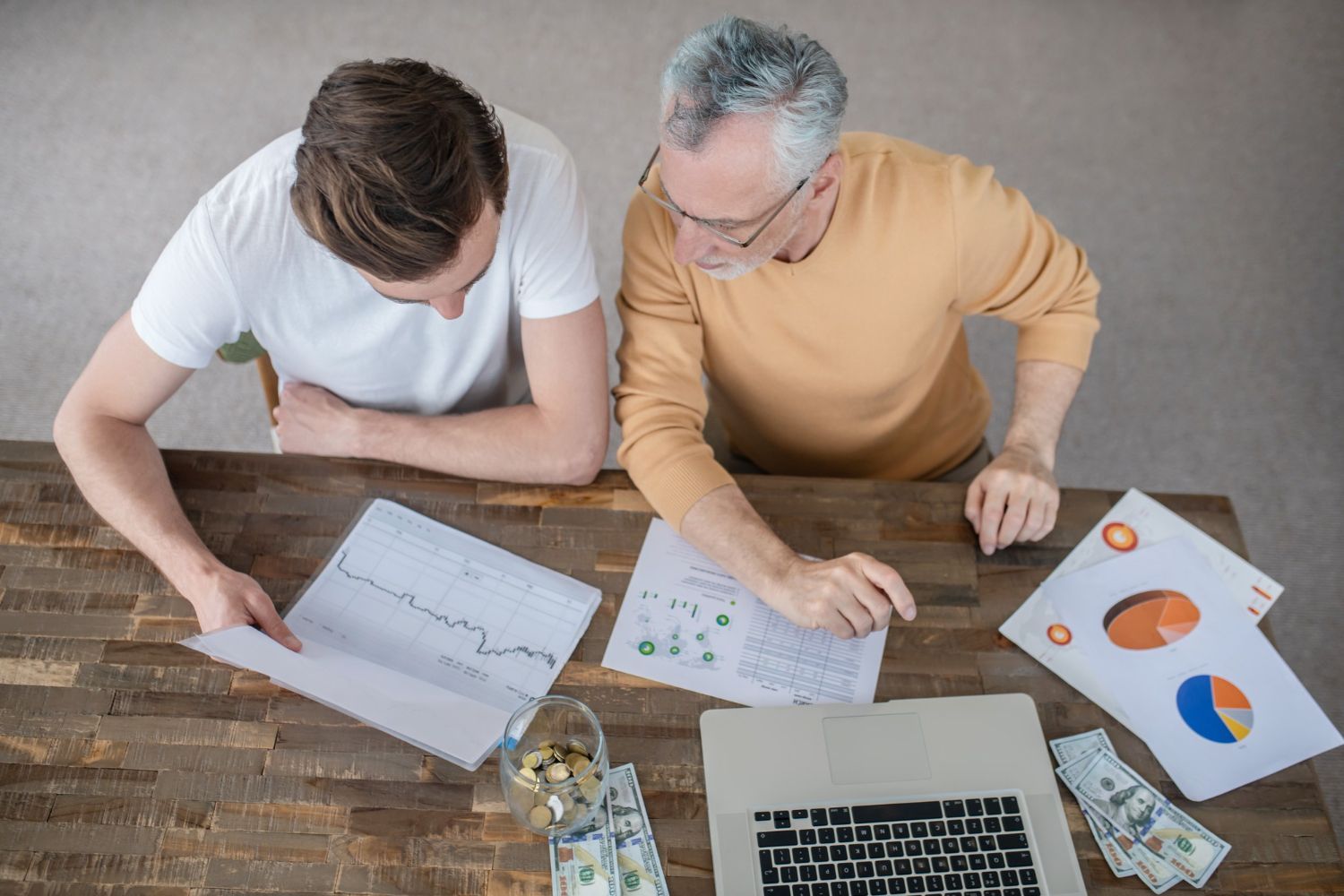 Two people reviewing charts and graphs at a desk with a laptop and papers