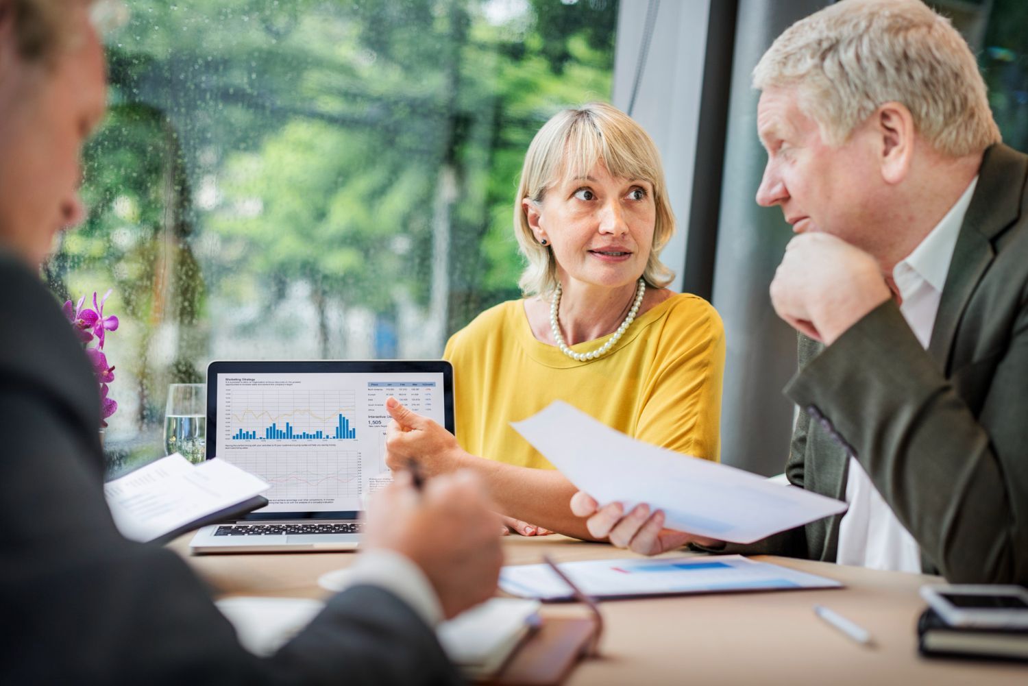 Business meeting with three people discussing documents beside a laptop showing charts