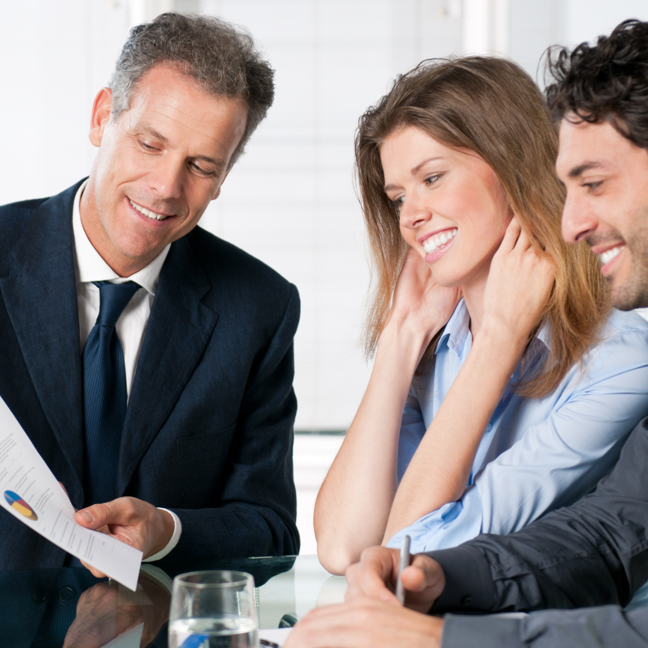 Three business people smiling and reviewing documents at a meeting table