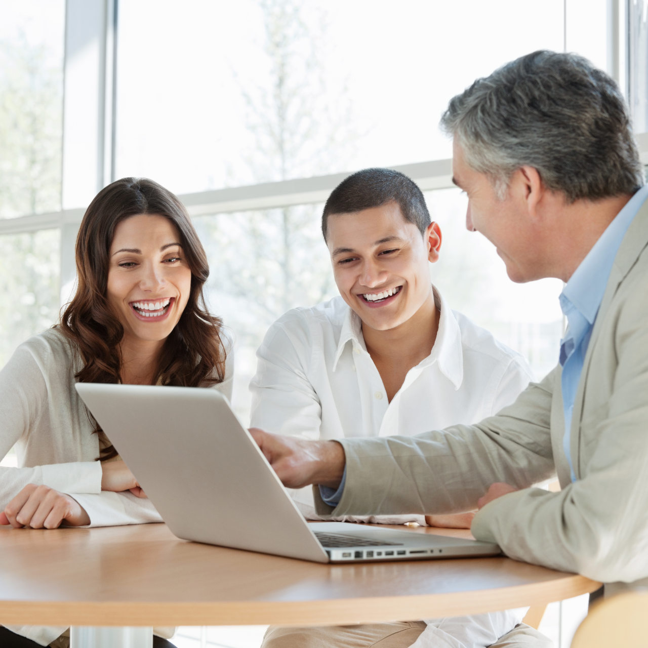 Three colleagues smiling around a laptop in a bright meeting room