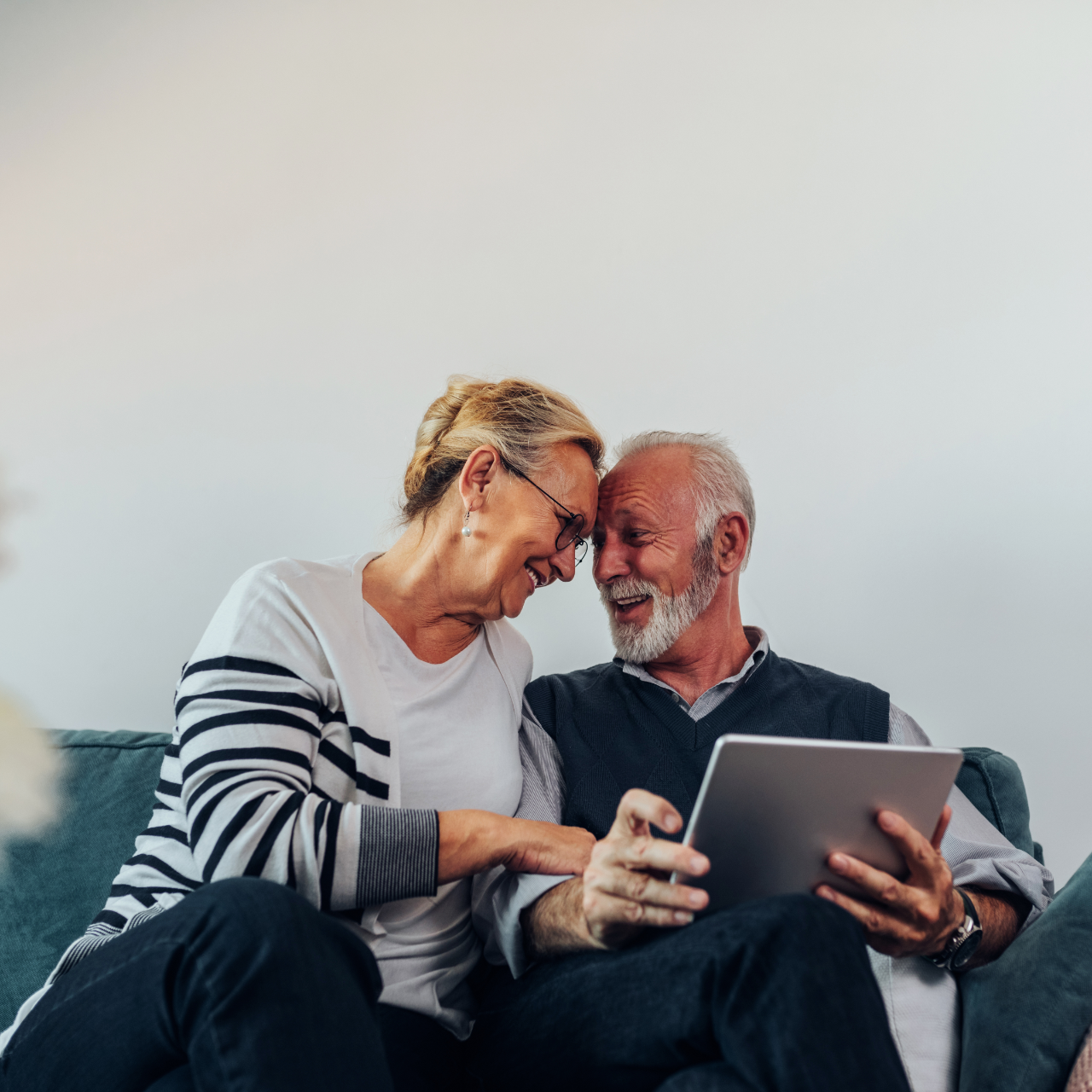 Two people smiling on a couch, looking at a tablet together