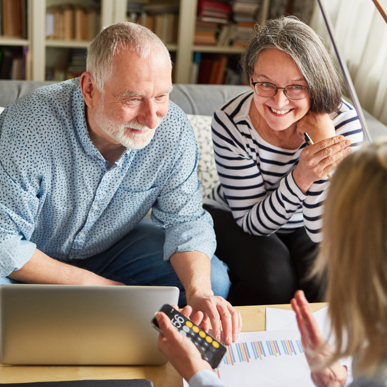 Smiling couple on a couch using a laptop and calculator while reviewing papers with a child nearby