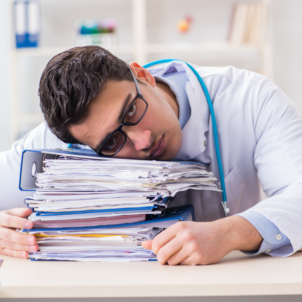 Tired office worker resting his head on a stack of files at a desk