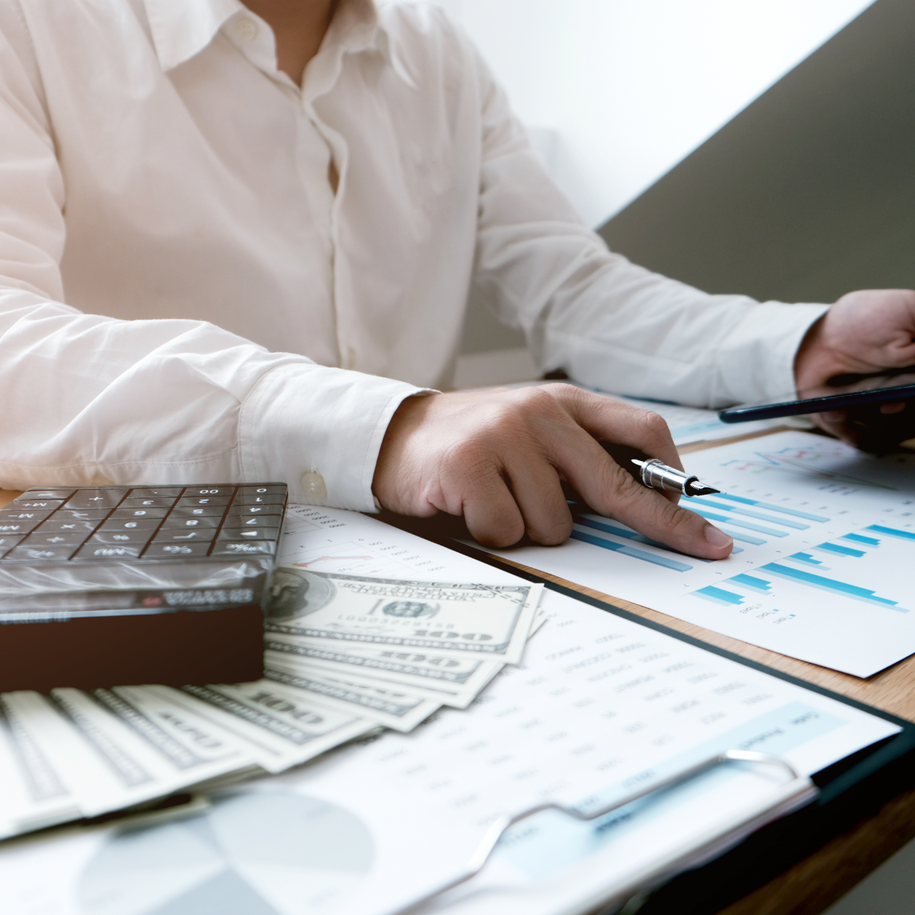 Person reviewing financial charts with calculator, cash, and documents on a desk