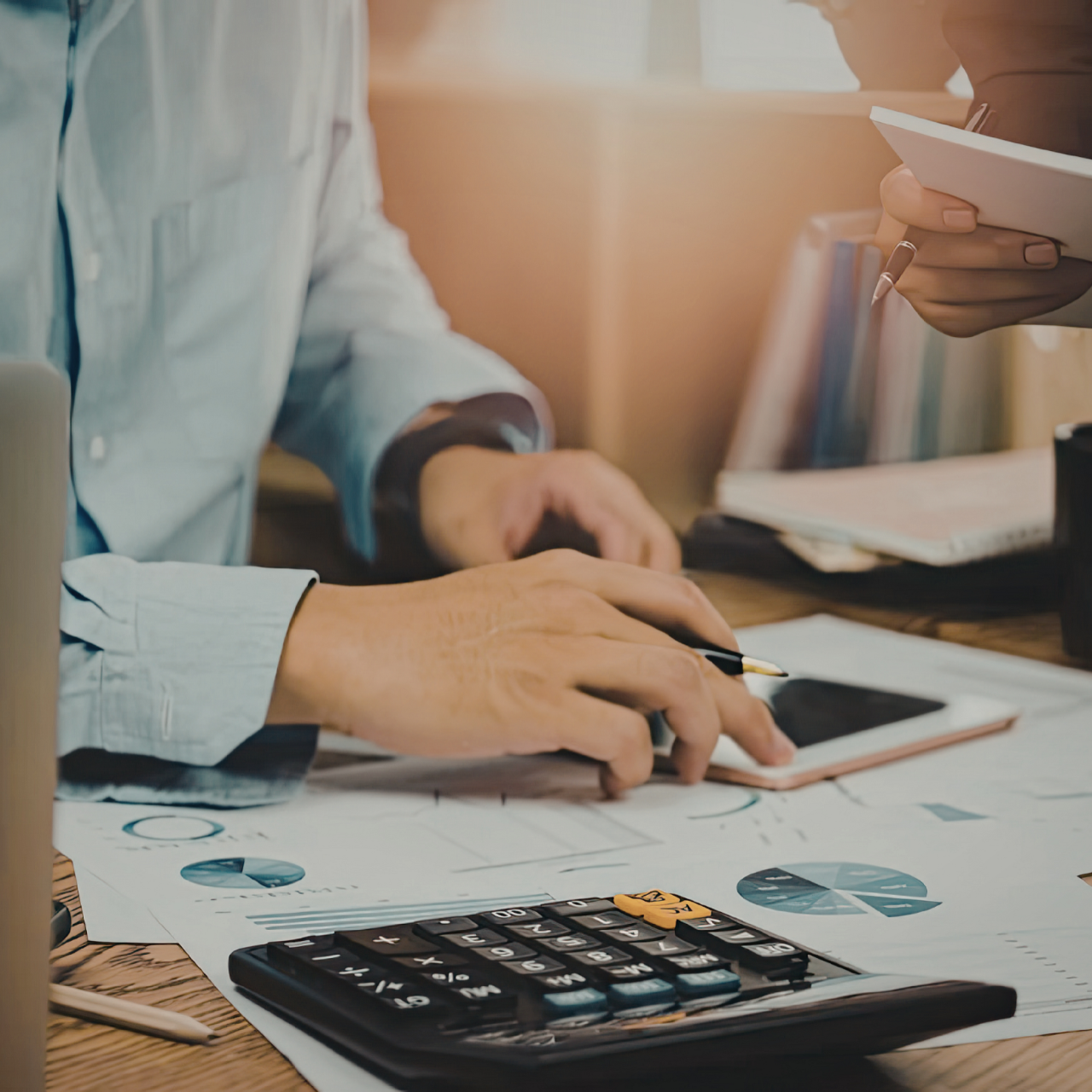 Hands using a calculator and tablet on a desk with charts during a business meeting