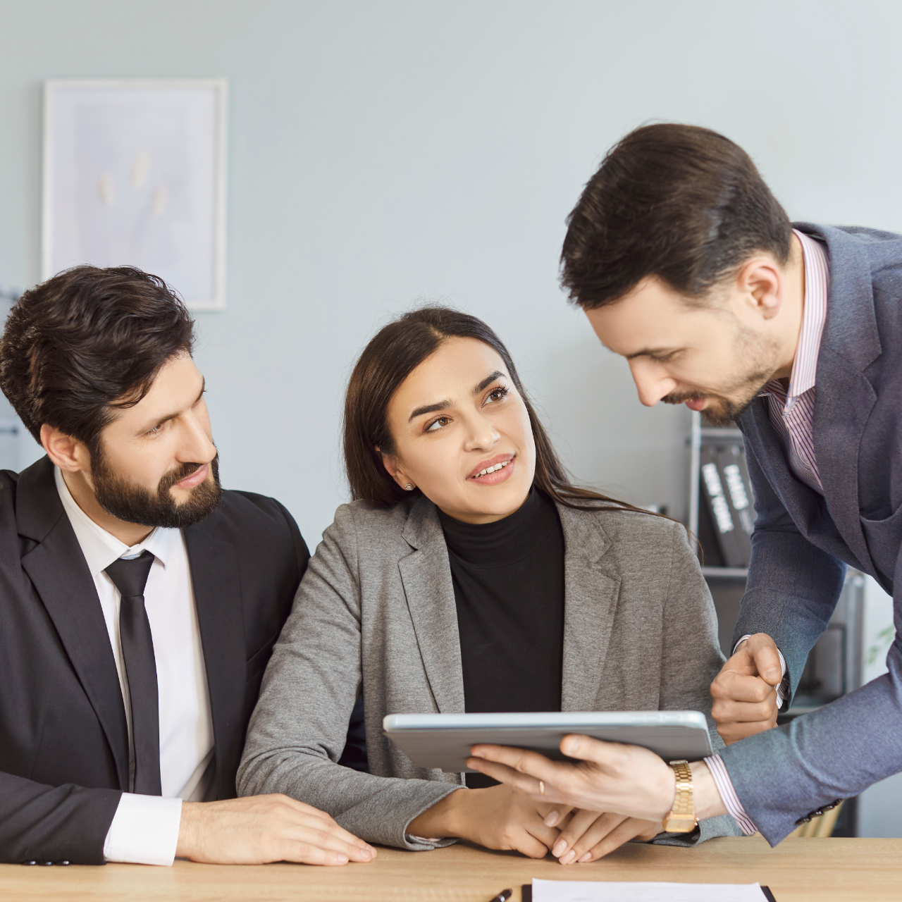 Three colleagues in a meeting, discussing a tablet at a desk