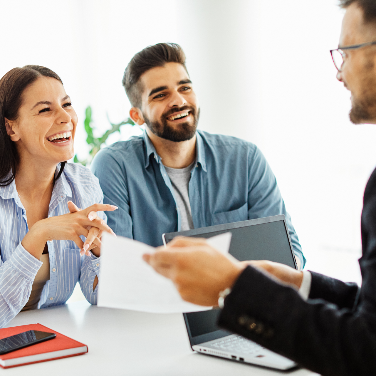 Three coworkers smiling during a meeting, with a laptop and papers on a table