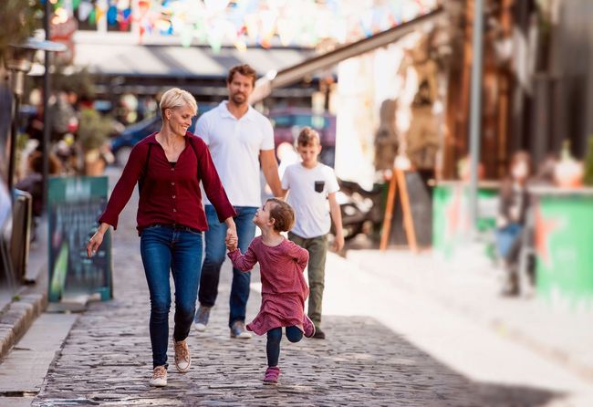 Family walking hand in hand down a cobblestone street with colorful shops in the background