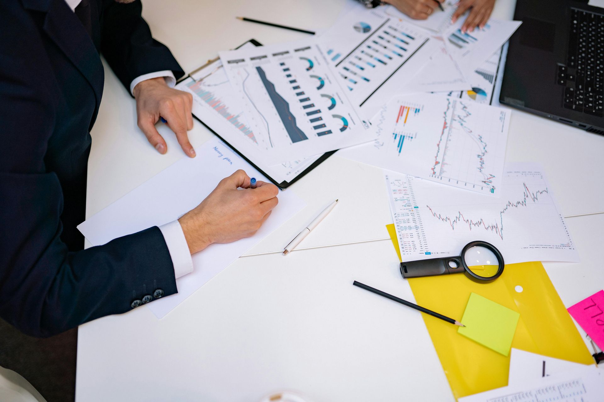 Business meeting with hands reviewing charts, graphs, and documents on a white table