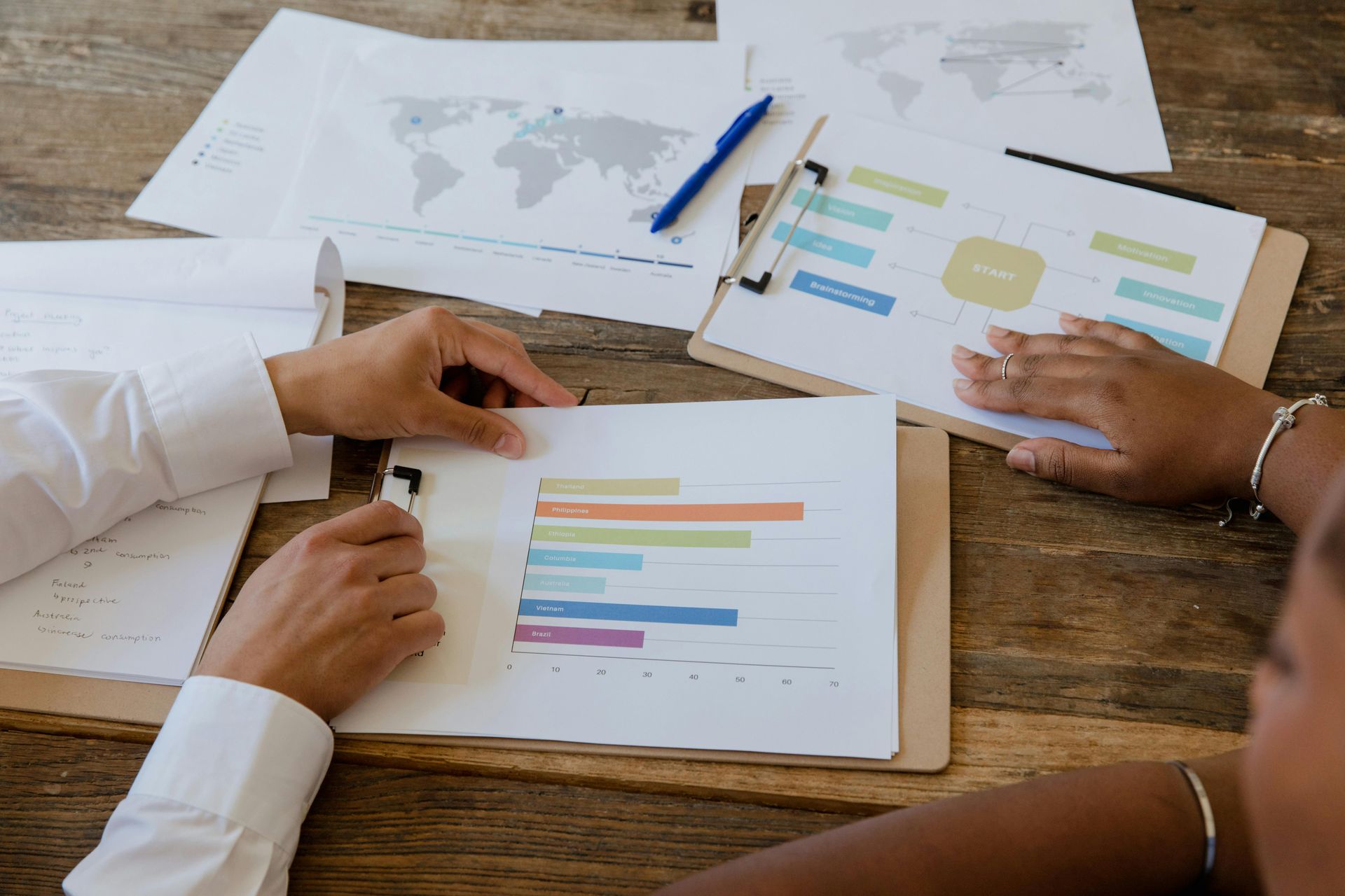 Hands pointing at printed charts and graphs on a wooden table during a business meeting